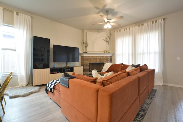 living room featuring ceiling fan, a fireplace, and light wood-type flooring