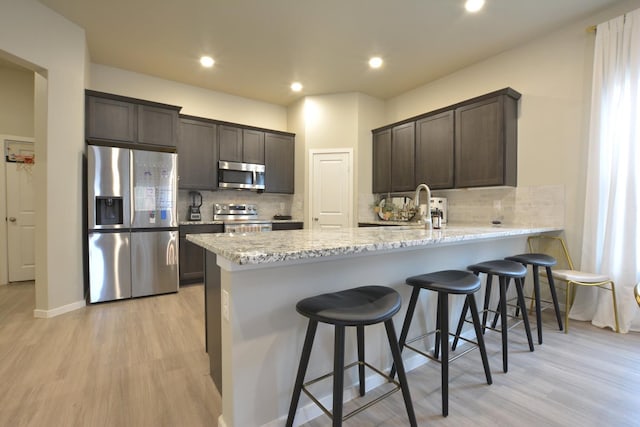 kitchen featuring sink, light hardwood / wood-style flooring, dark brown cabinets, stainless steel appliances, and light stone countertops