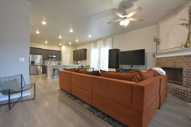 living room with ceiling fan, a fireplace, and light wood-type flooring