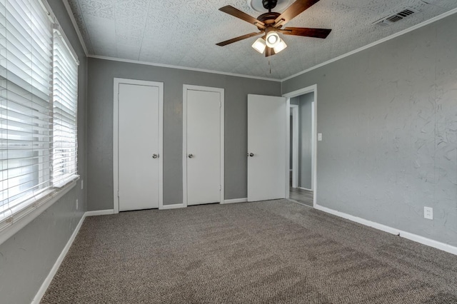 unfurnished bedroom featuring crown molding, carpet floors, a textured ceiling, and two closets