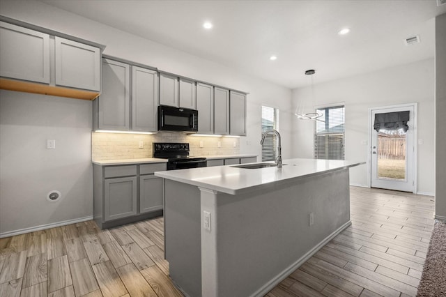 kitchen with gray cabinets, decorative light fixtures, sink, a kitchen island with sink, and black appliances