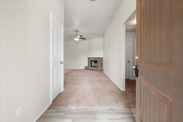 unfurnished living room with a fireplace, light colored carpet, and ceiling fan