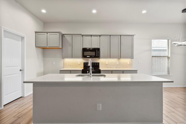 kitchen with tasteful backsplash, sink, black appliances, and an island with sink