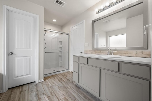 bathroom with wood-type flooring, a shower with shower door, vanity, and backsplash