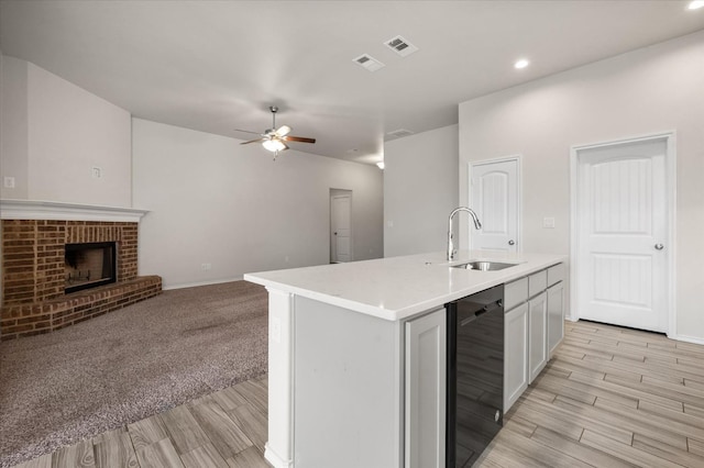 kitchen with a fireplace, an island with sink, black dishwasher, sink, and ceiling fan