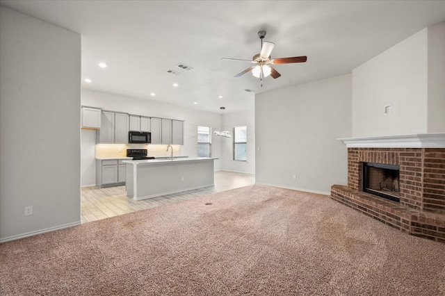 unfurnished living room featuring ceiling fan, a brick fireplace, sink, and light carpet