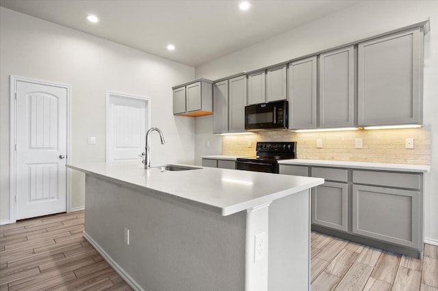 kitchen featuring gray cabinets, tasteful backsplash, an island with sink, sink, and black appliances