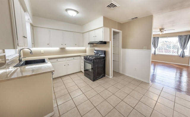 kitchen featuring light tile patterned flooring, sink, white cabinetry, black gas range oven, and ceiling fan