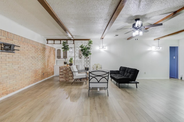 living area featuring light hardwood / wood-style flooring, ceiling fan, a textured ceiling, brick wall, and beamed ceiling