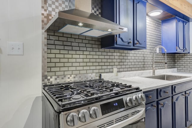 kitchen featuring blue cabinetry, stainless steel gas stove, sink, and wall chimney range hood