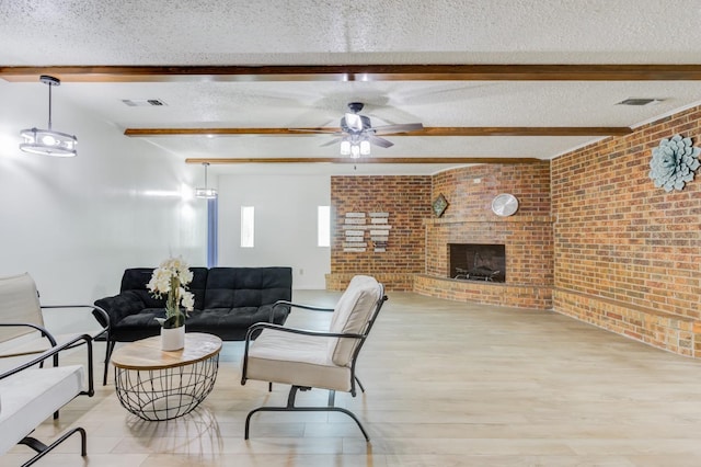 living room with light hardwood / wood-style floors, a textured ceiling, brick wall, a brick fireplace, and beamed ceiling