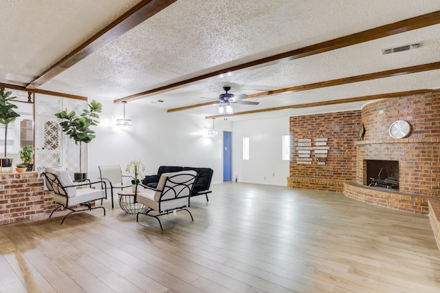 living area with a textured ceiling, light wood-type flooring, beamed ceiling, brick wall, and a fireplace