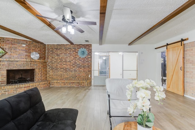 living room featuring beam ceiling, a fireplace, a textured ceiling, a barn door, and light wood-type flooring