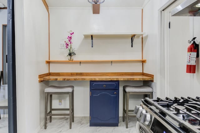 kitchen with blue cabinets, butcher block countertops, stainless steel gas stove, crown molding, and built in desk