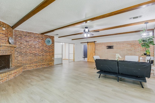 living room featuring a fireplace, a barn door, a textured ceiling, beam ceiling, and light hardwood / wood-style flooring