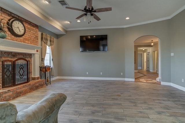 living room with a brick fireplace, crown molding, and ceiling fan