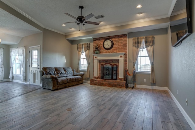 unfurnished living room featuring a fireplace, wood-type flooring, ornamental molding, ceiling fan, and a textured ceiling