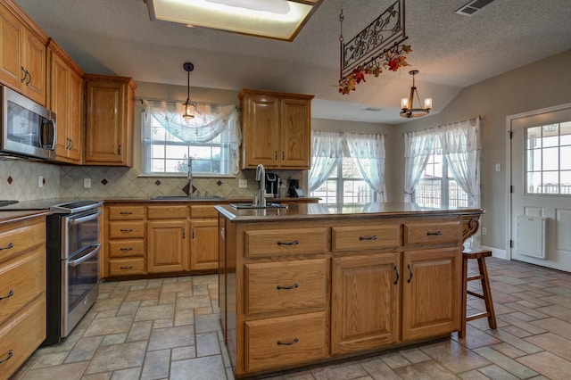 kitchen with hanging light fixtures, appliances with stainless steel finishes, sink, and a center island with sink