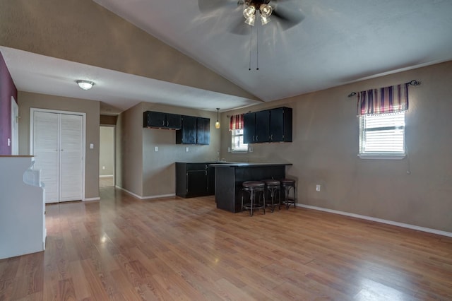 kitchen with lofted ceiling, sink, a kitchen breakfast bar, ceiling fan, and light hardwood / wood-style flooring