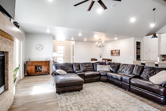 living room featuring ceiling fan with notable chandelier, a fireplace, vaulted ceiling, and light wood-type flooring