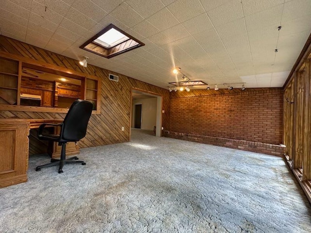 unfurnished office featuring track lighting, wooden walls, carpet, and brick wall