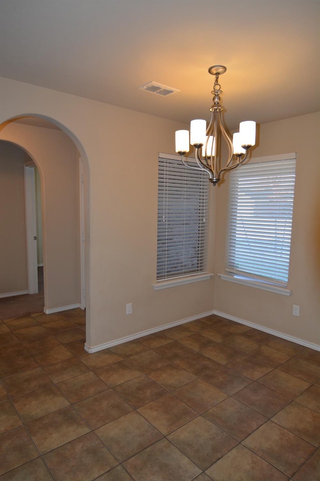 tiled spare room featuring an inviting chandelier