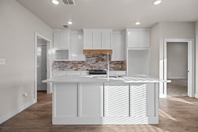 kitchen with tasteful backsplash, white cabinetry, hardwood / wood-style floors, and a center island with sink