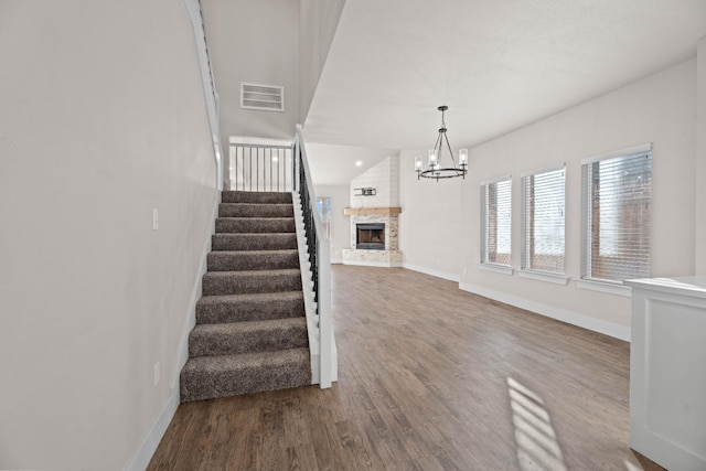 staircase featuring vaulted ceiling, a fireplace, a chandelier, and hardwood / wood-style floors