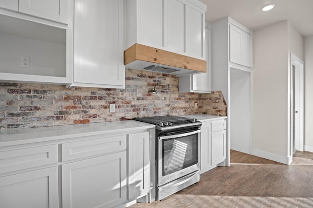 kitchen featuring ventilation hood, white cabinetry, tasteful backsplash, hardwood / wood-style flooring, and stainless steel gas range