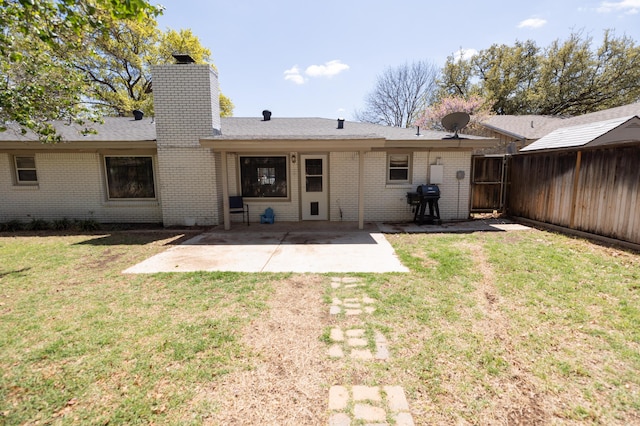rear view of house featuring a chimney, a yard, brick siding, fence, and a patio
