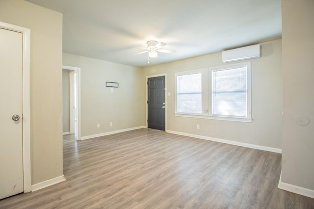 empty room with ceiling fan, a wall unit AC, and light wood-type flooring