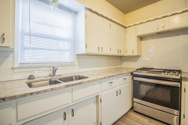 kitchen with white cabinets, sink, stainless steel gas range, and backsplash