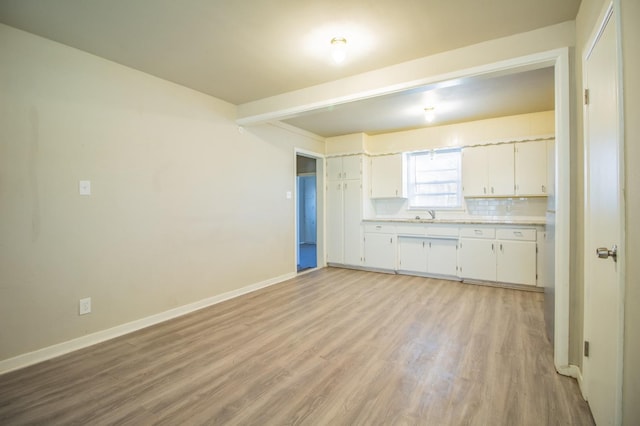 kitchen with beamed ceiling, white cabinetry, sink, backsplash, and light wood-type flooring