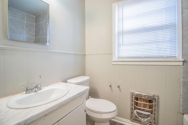 bathroom featuring vanity, heating unit, and toilet