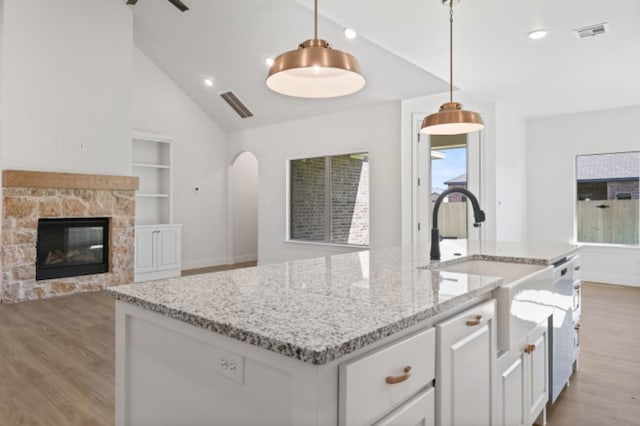 kitchen featuring sink, white cabinetry, light wood-type flooring, an island with sink, and pendant lighting