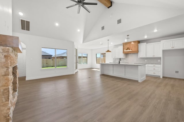 kitchen with white cabinetry, hanging light fixtures, tasteful backsplash, wood-type flooring, and a center island with sink