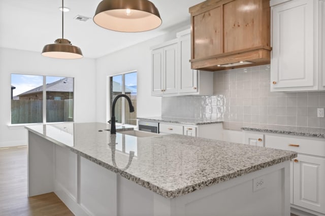 kitchen featuring decorative light fixtures, white cabinetry, sink, light stone counters, and light hardwood / wood-style flooring