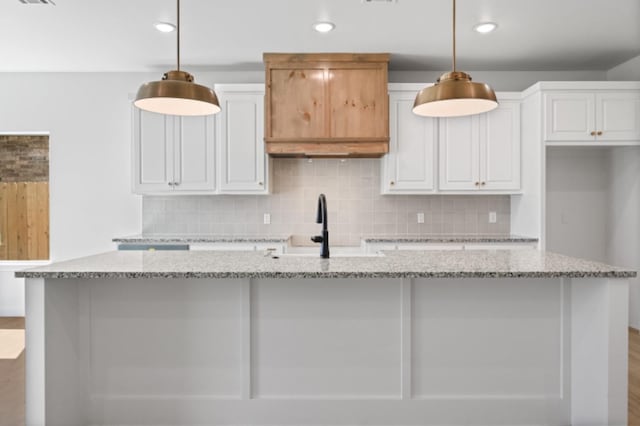 kitchen with white cabinetry, decorative light fixtures, a kitchen island with sink, and light stone countertops