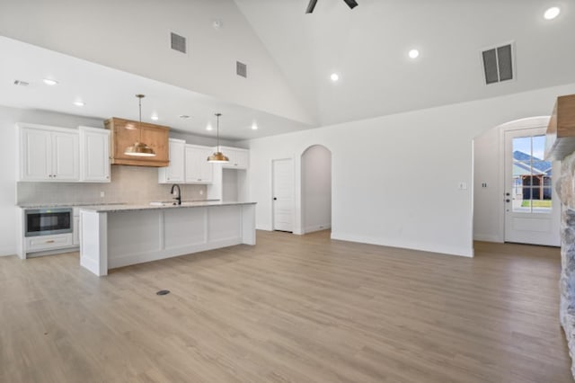 kitchen with sink, white cabinetry, hanging light fixtures, a kitchen island with sink, and built in microwave