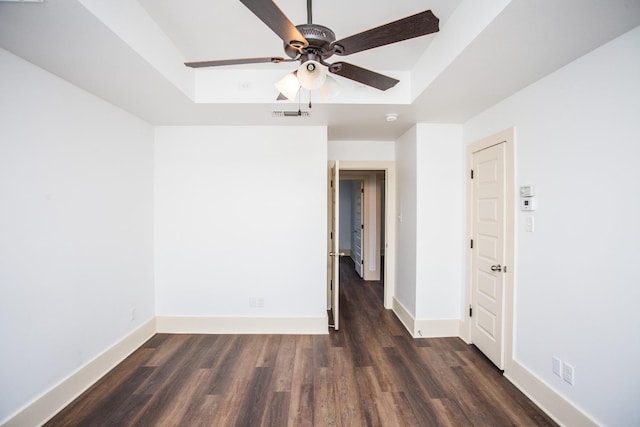 empty room with a raised ceiling, ceiling fan, and dark hardwood / wood-style flooring