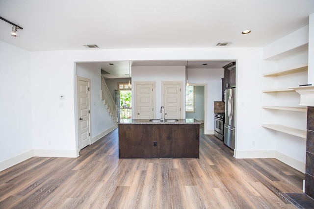 kitchen featuring sink, dark wood-type flooring, appliances with stainless steel finishes, a kitchen island with sink, and dark brown cabinetry