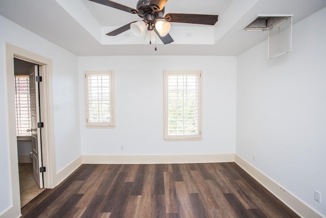 spare room featuring dark hardwood / wood-style floors, a wealth of natural light, ceiling fan, and a tray ceiling