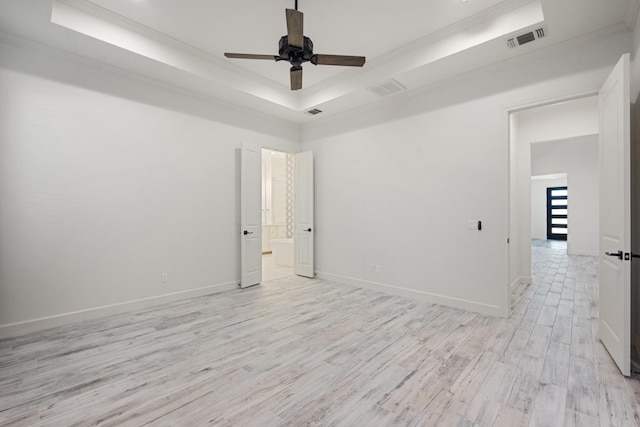 empty room featuring light wood finished floors, visible vents, a raised ceiling, and ornamental molding