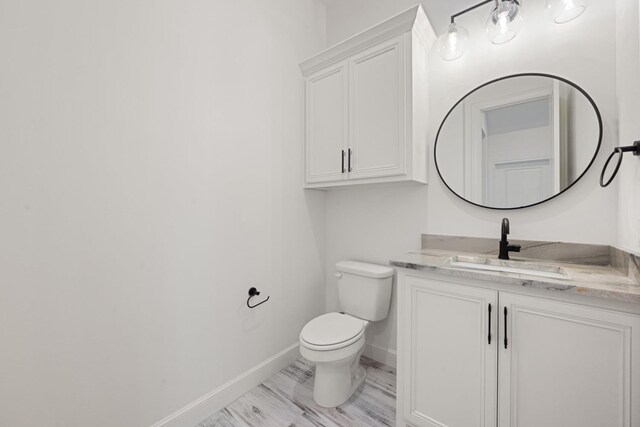 half bath with baseboards, toilet, and vanity