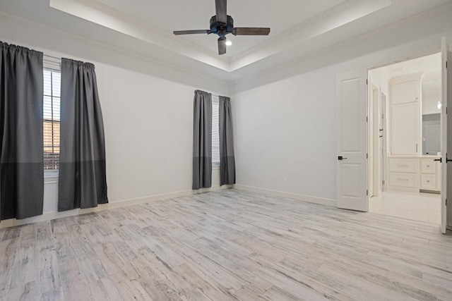 empty room featuring a raised ceiling, crown molding, baseboards, and light wood-type flooring