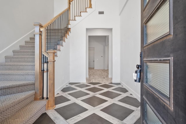 entryway with stairs, a high ceiling, visible vents, and baseboards