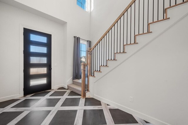 foyer entrance with stairs, a high ceiling, and baseboards