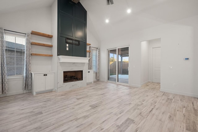 unfurnished living room with a wealth of natural light, light wood-style floors, high vaulted ceiling, and a high end fireplace