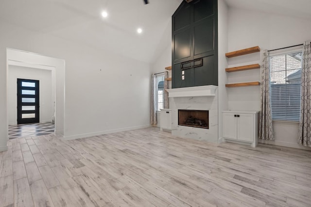 unfurnished living room featuring light wood finished floors, baseboards, a premium fireplace, recessed lighting, and high vaulted ceiling