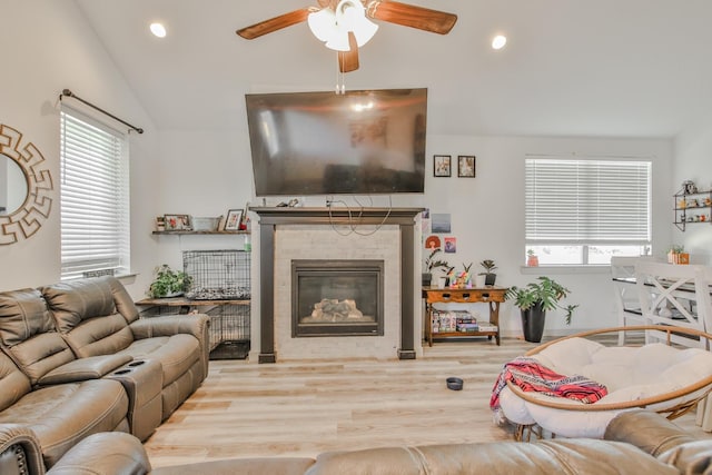 living room with a tiled fireplace, vaulted ceiling, ceiling fan, and light wood-type flooring